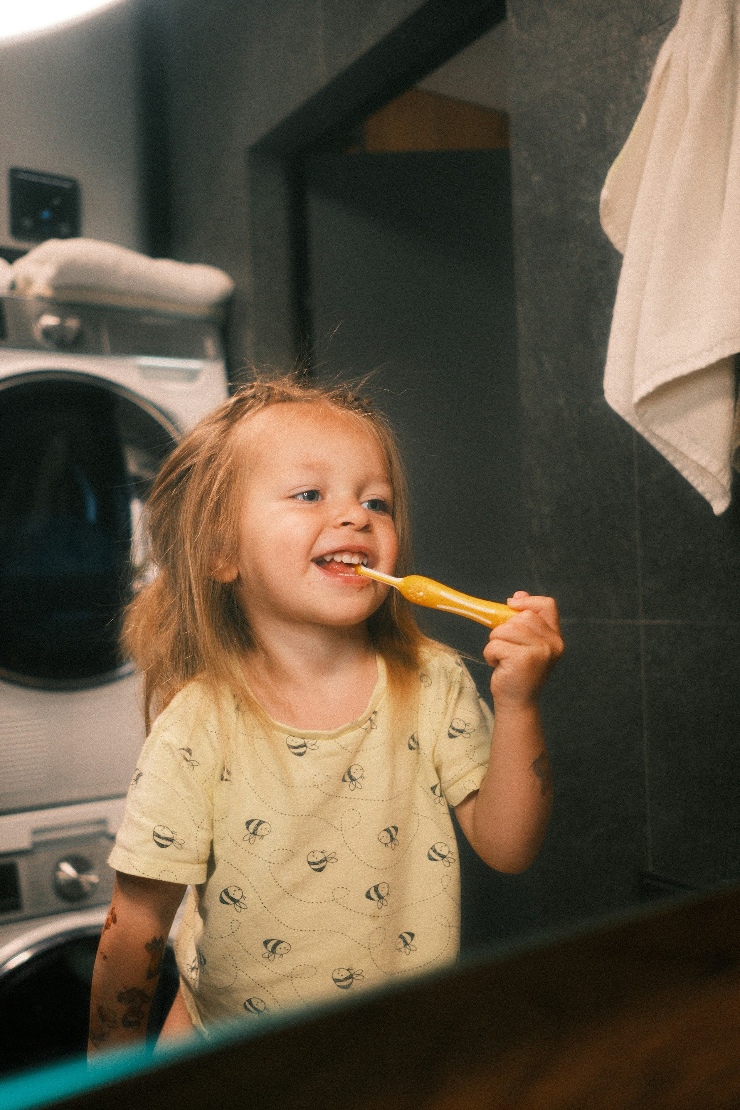 Young girl smiling as she brushes her teeth in the mirror