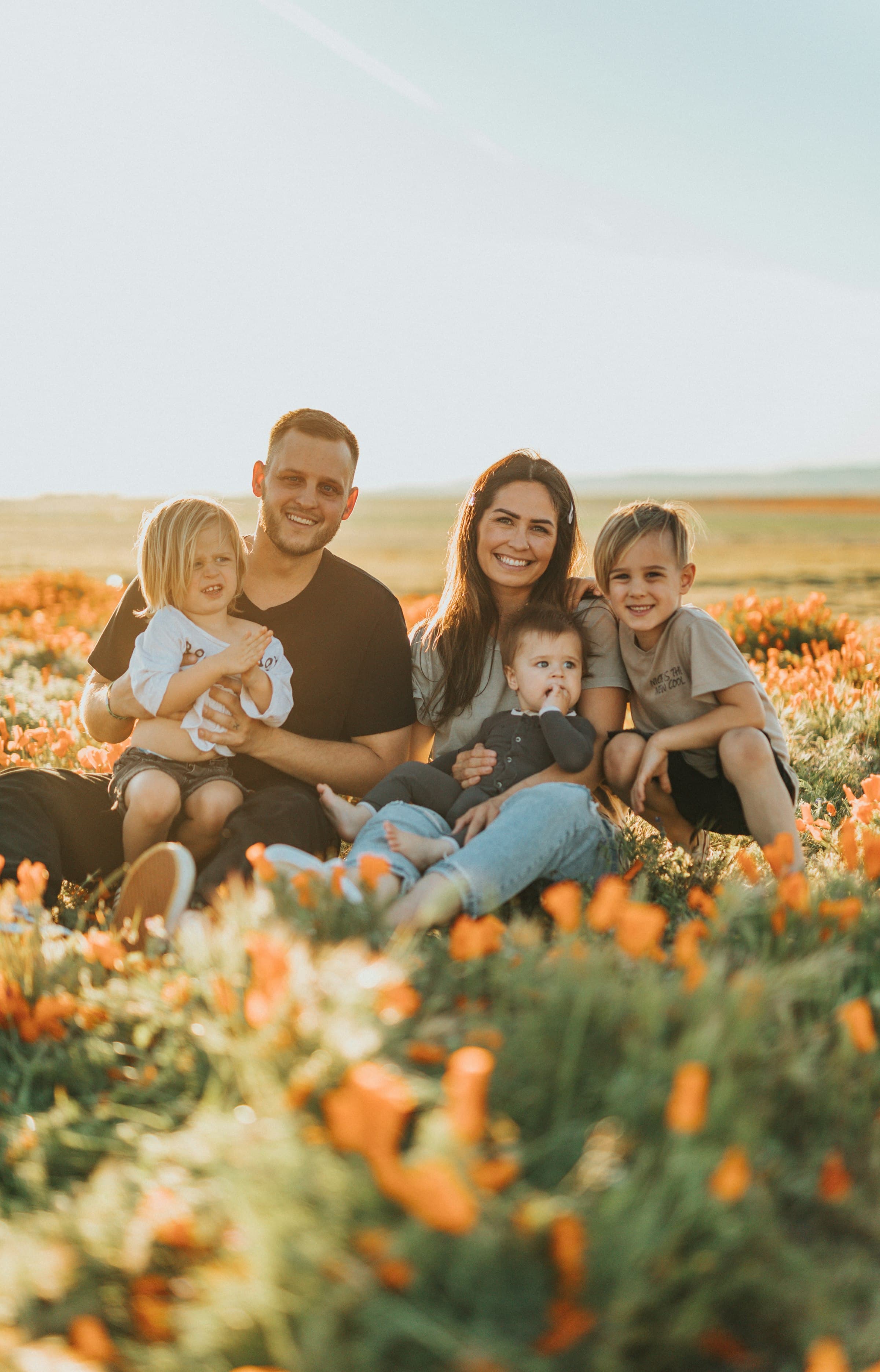 Smiling family of five sitting in a field of orange poppies